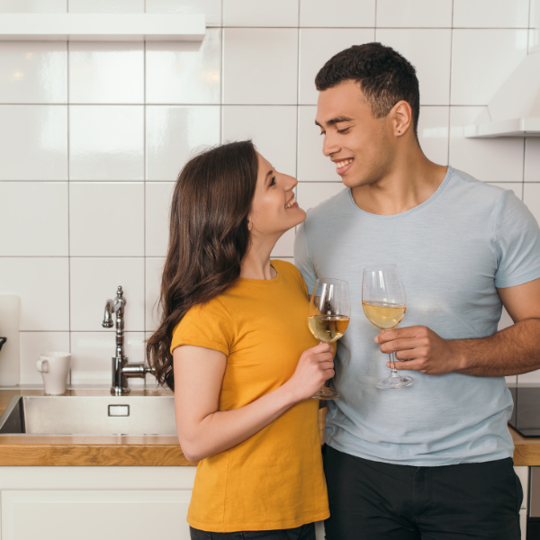 A mixed race couple smile and share a bottle of wine to celebrate their engagement