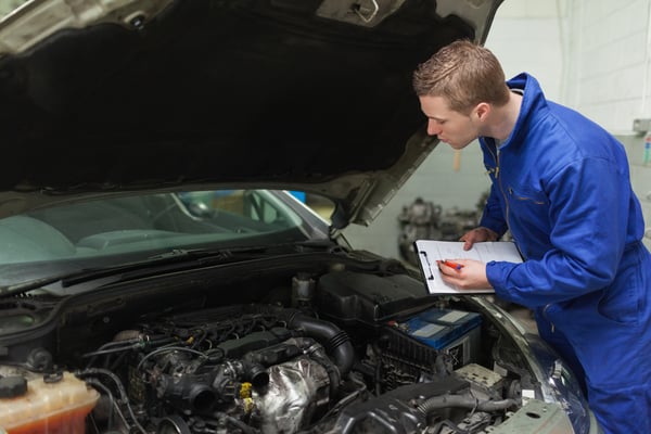 Male mechanic writing on clipboard while examining car engine