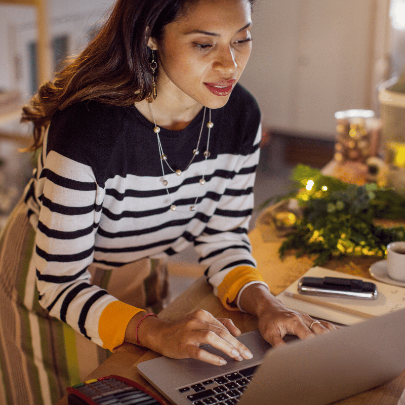 young woman in striped sweater shopping from laptop during holiday season