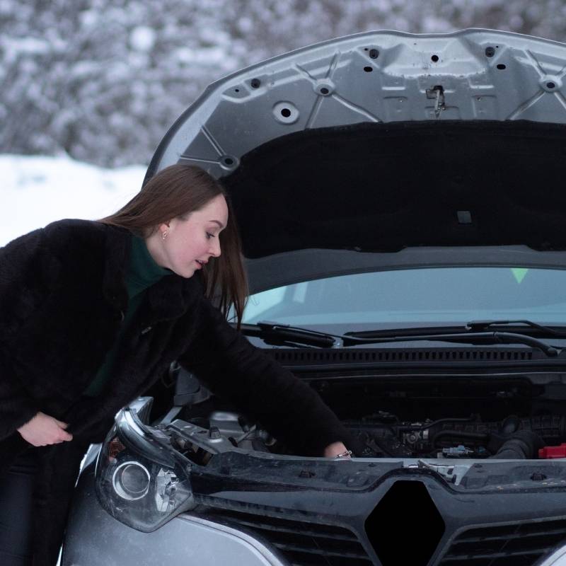 woman checking oil of black car in winter