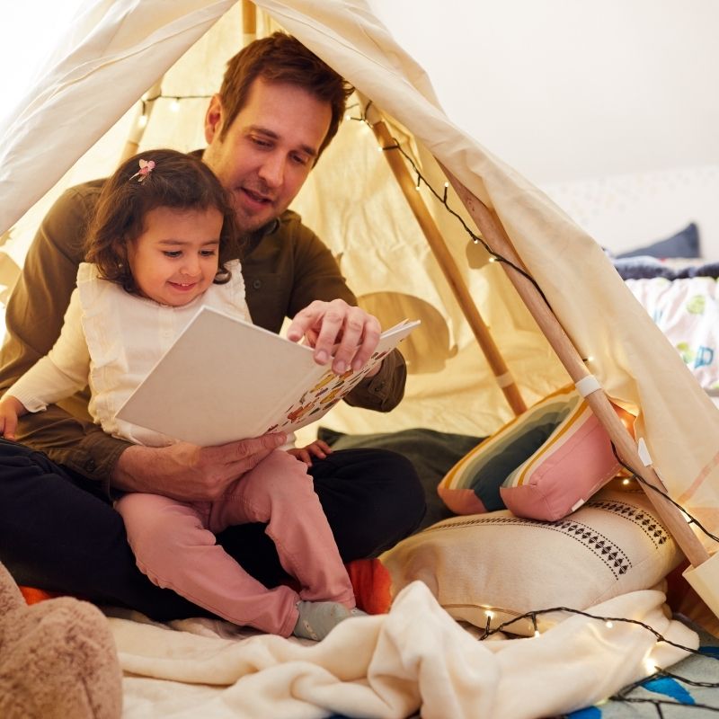 father with young daughter in indoor tent reading a book