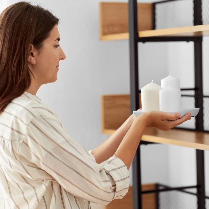 woman staging home placing white candles on a wooden shelf
