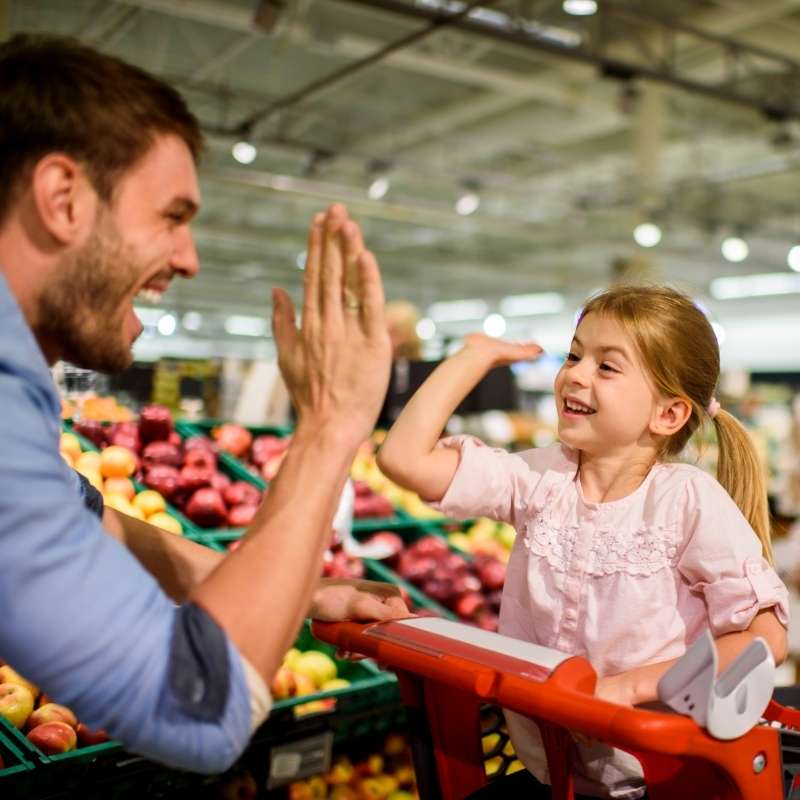 father giving daughter in shopping carriage a high five at the grocery store