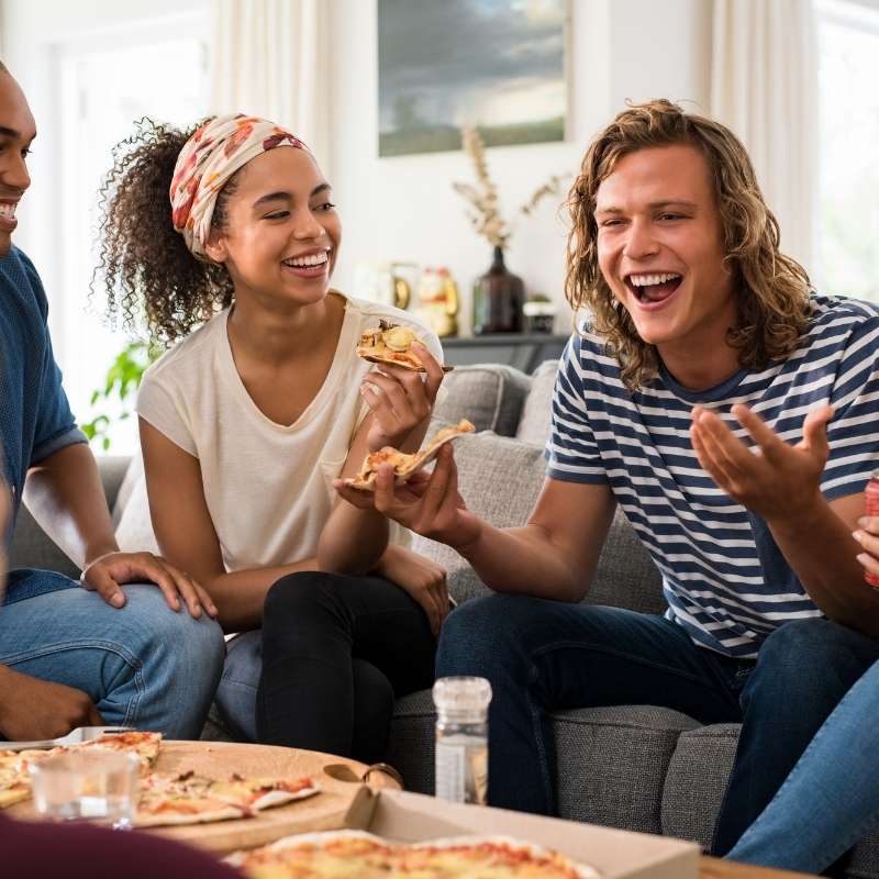 young people on couch eating pizza in new home