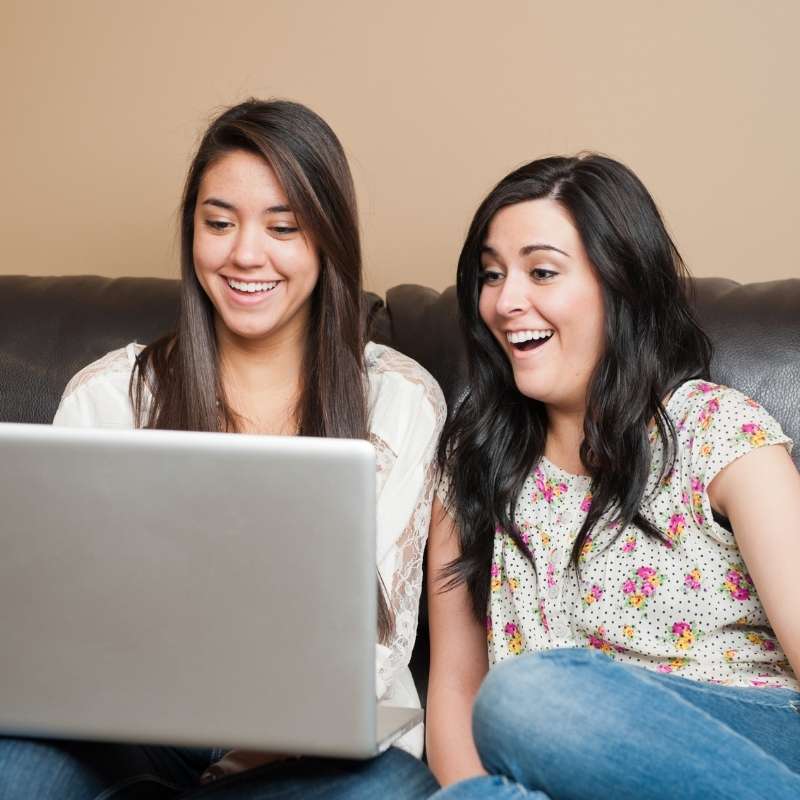 two young women on couch looking at social media quiz scam