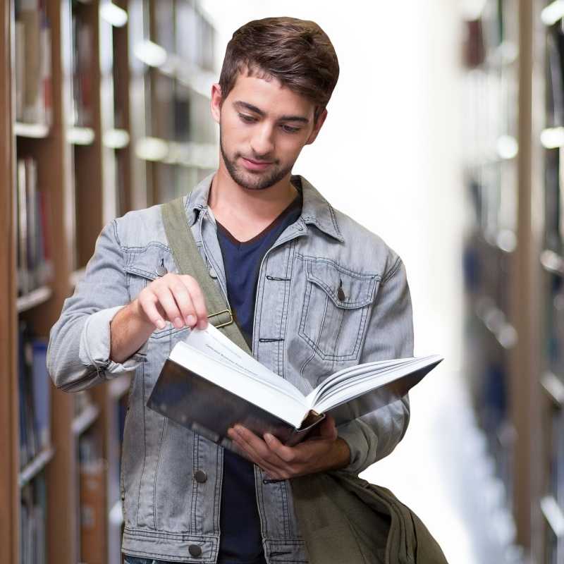male college student looking at book in library stacks