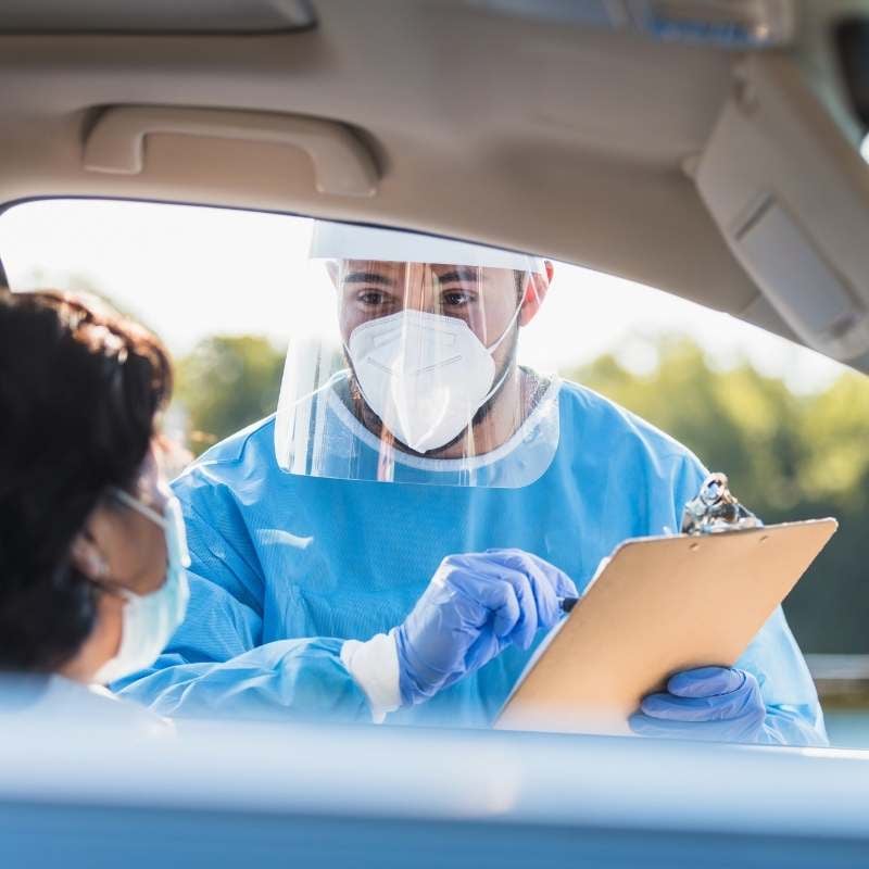 male nurse standing outside car taking info from woman for COVID-19 test