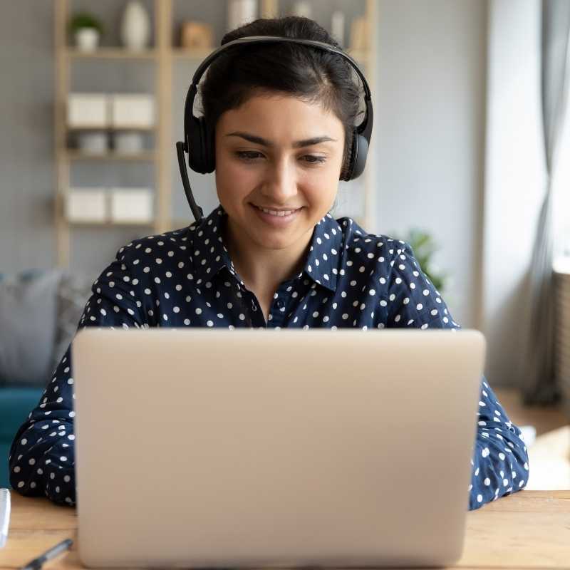 young woman at desk looking at webinar on laptop