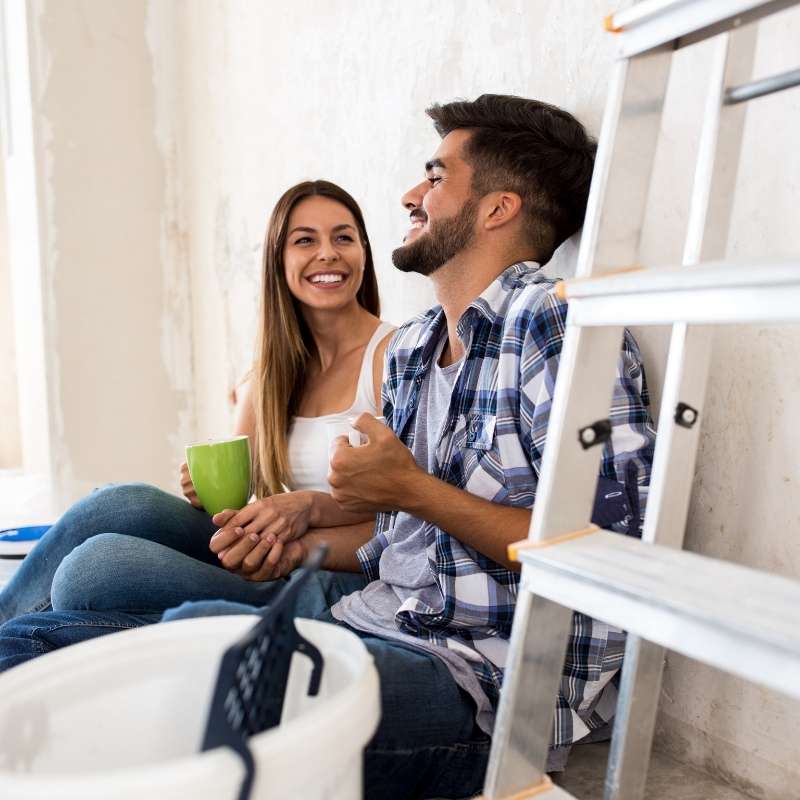 man and woman drinking from mugs sitting next to ladder in a home renovation