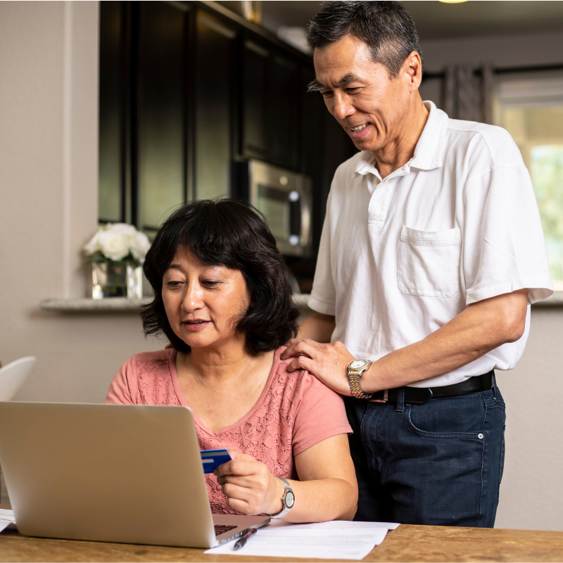An older Asian couple are looking up their credit card's interest rate and payoff information on their laptop. 