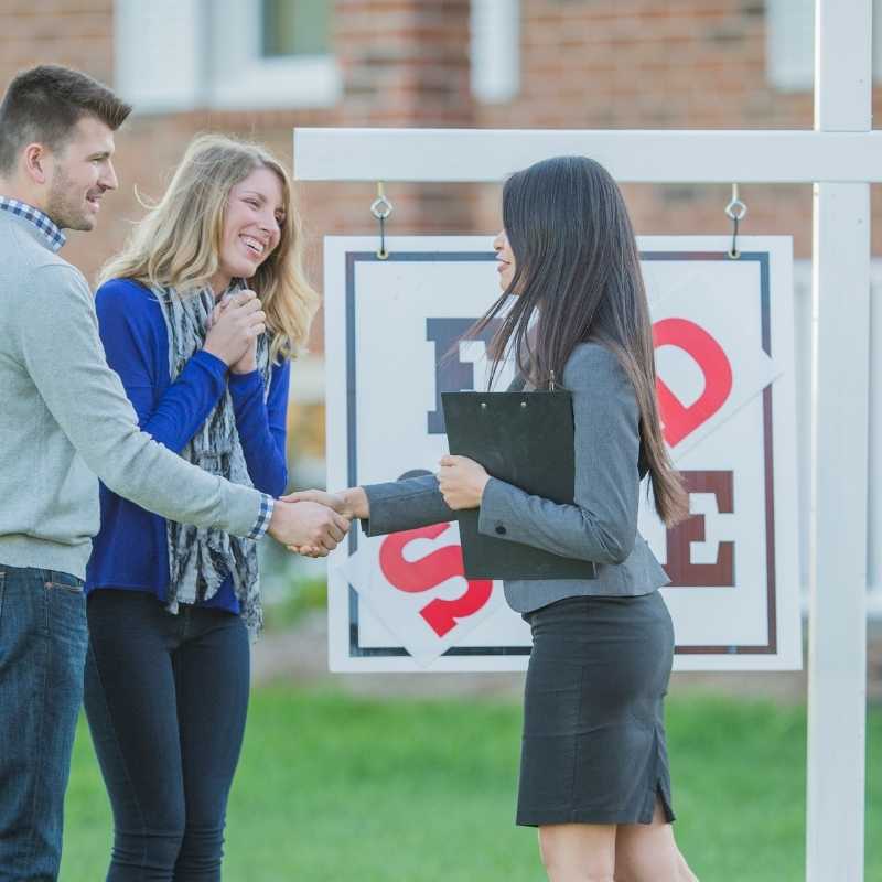 young couple buying first home shaking hands with Realtor 