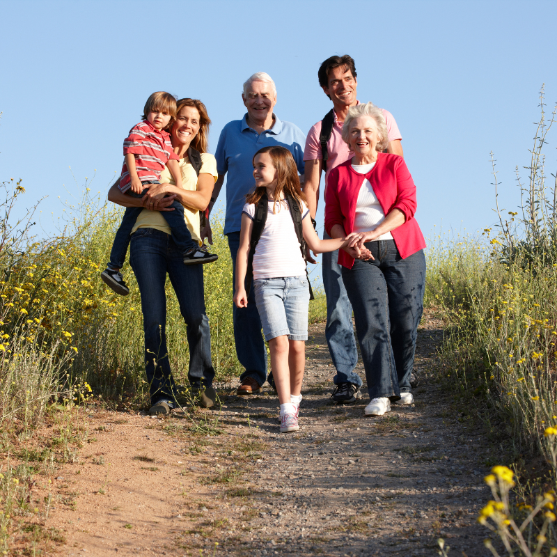 Three generations of a white family take a walk through a path in a field. 