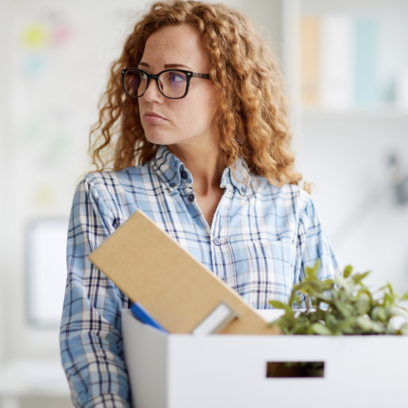 woman with curly red hair holding box filled with office belongings after unexpected job loss