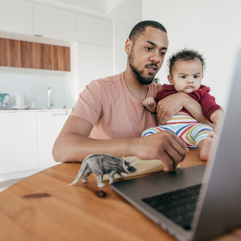 father paying bills with baby on desk in front of laptop