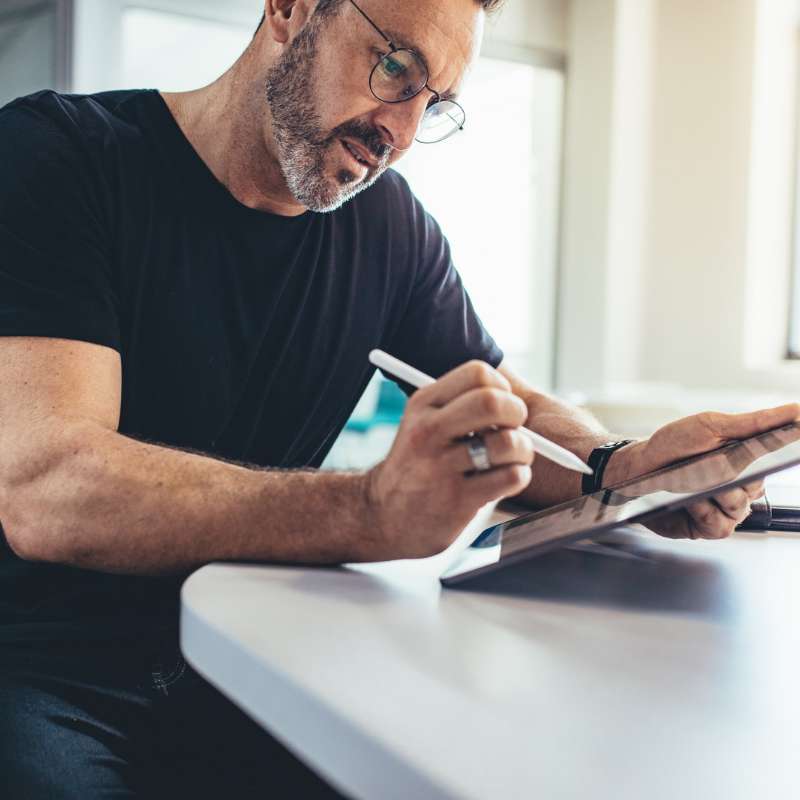 older man using digital pencil on electronic tablet on white countertop