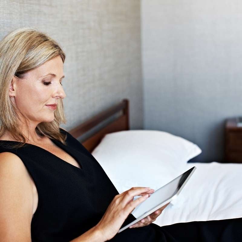 blonde middle aged woman on bed looking at mortgage rates on tablet