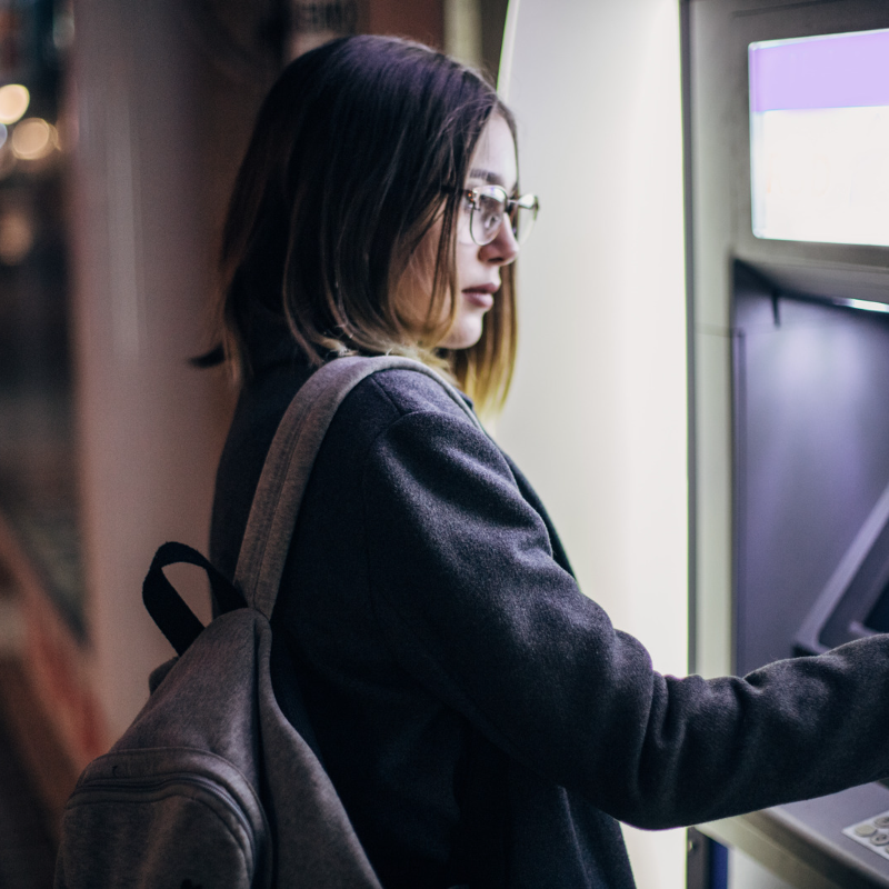 young Asian woman standing in front of a no fee ATM machine withdrawing cash 